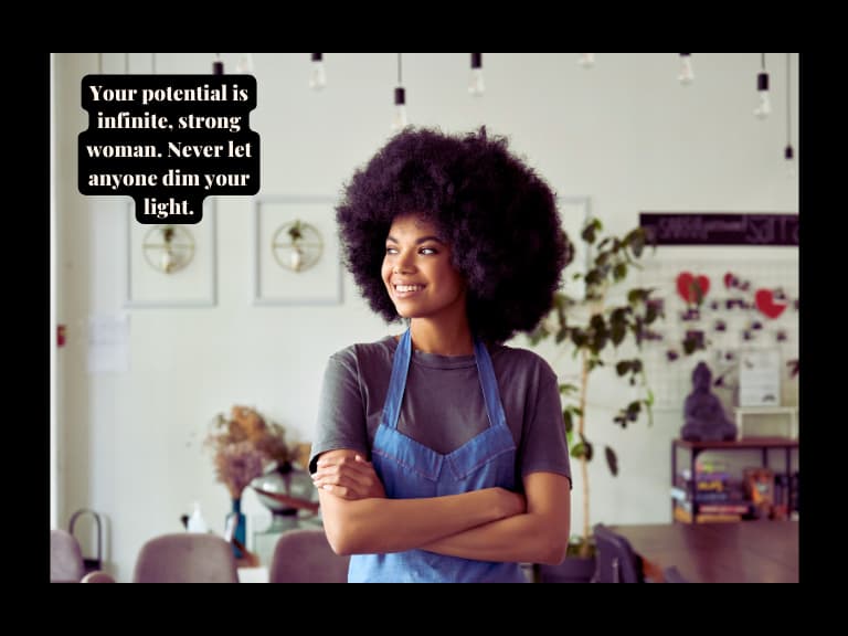 A black independent  strong woman looking out of the window smiling with a blue apron and a grey t shirt and afro hair